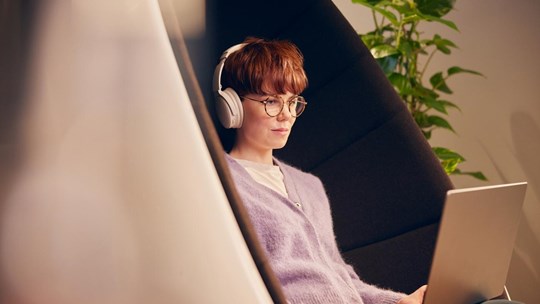 A young woman in glasses working on her laptop wearing headphones 