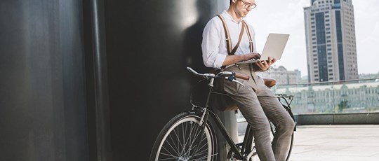 stylish young man working with laptop while leaning on vintage bicycle