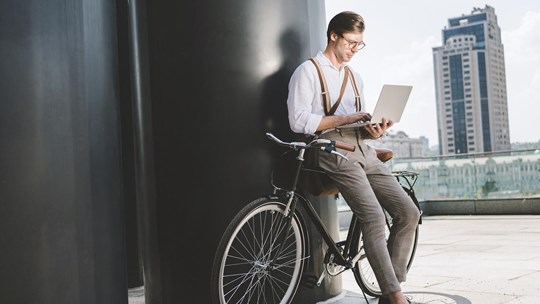 stylish young man working with laptop while leaning on vintage bicycle