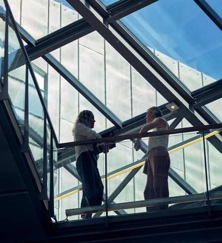 Two ladies talk standing in the skywalk in Tietoevry office
